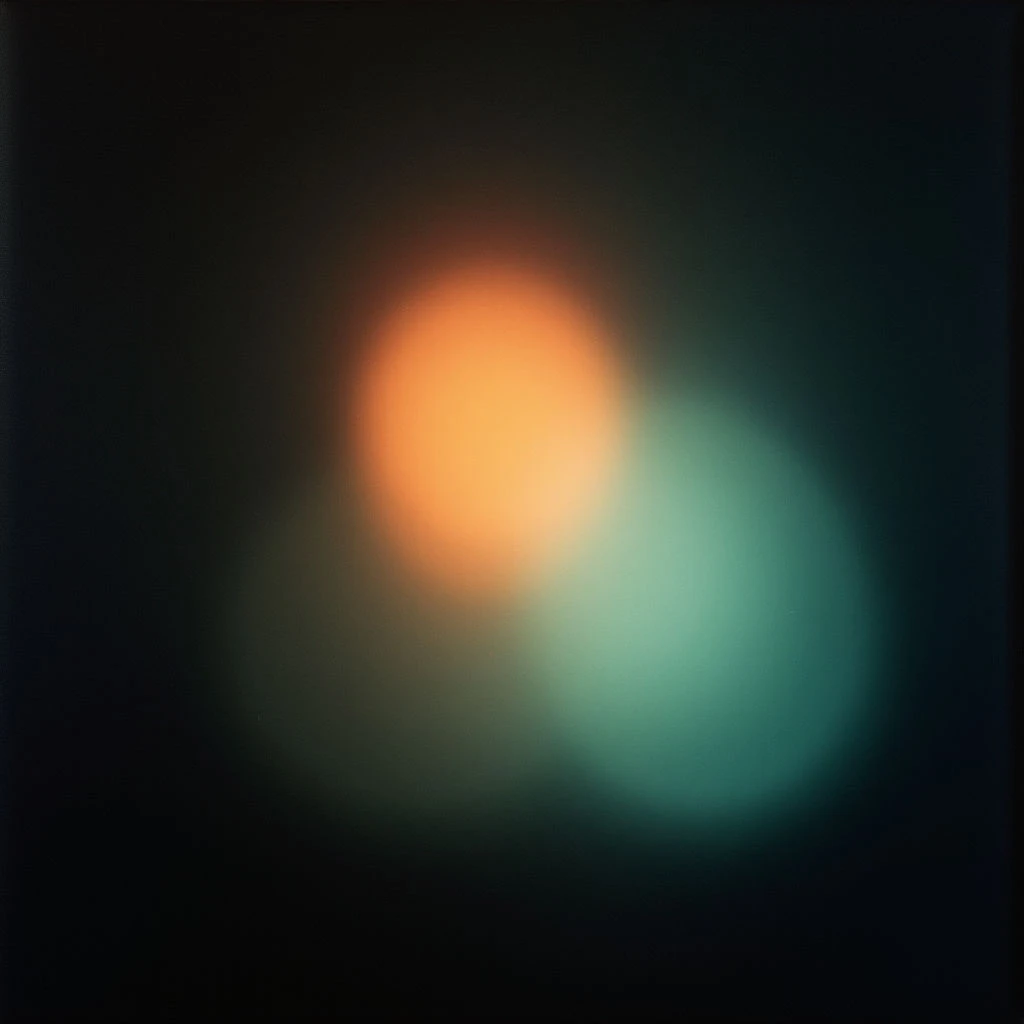 Two blurred orbs of color—one orange and one teal—float against a dark background. The shapes are soft-edged, blending slightly where they overlap, creating a hazy, indistinct form. It feels like looking at distant lights through a fog or a dreamlike abstraction.